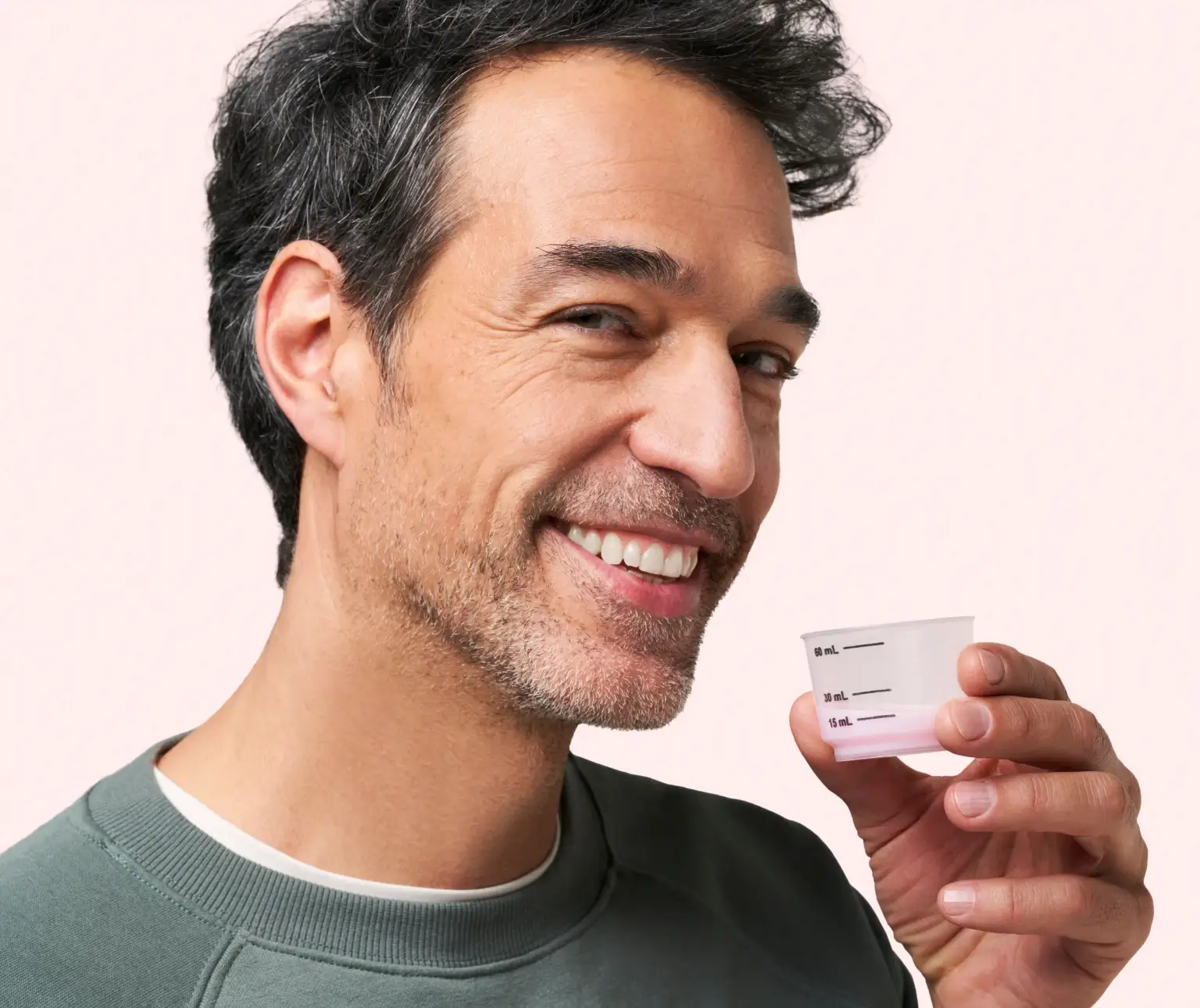 Smiling man holding a measuring cup with pink liquid.